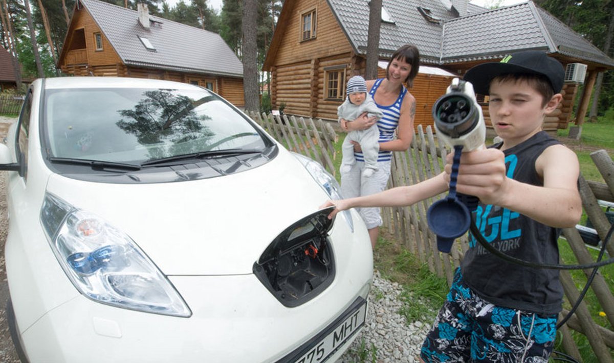 Annika Raidla näitab elektriautot, laadijaga vehib 11-aastane Sammo ja süles on seitsmekuune Jacob Georg.