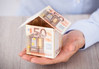 Businessman's,Hand,Holding,House,Made,Of,Euro,Notes,On,Table