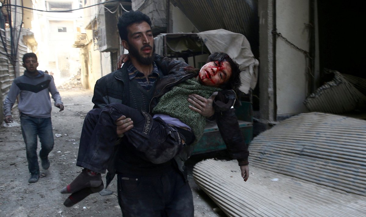 FILE PHOTO: Mohammed Abu Anas runs with an injured boy in the besieged eastern Ghouta town of Hamouriyeh near Damascus, Syria
