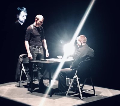 Stseen eskiisist “Pornojeesus”. Istub tegelane nimega Härg (Andres Mähar) ja tema ees seisab tegelane nimega Inimene (Tõnn Lamp). Ülekuulamist salvestab kaamera, mille pilt on projitseeritud seinale