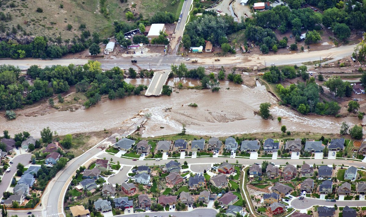 An aerial view shows flood waters and a washed-out road adjacent a suburban neighborhood in Lyons