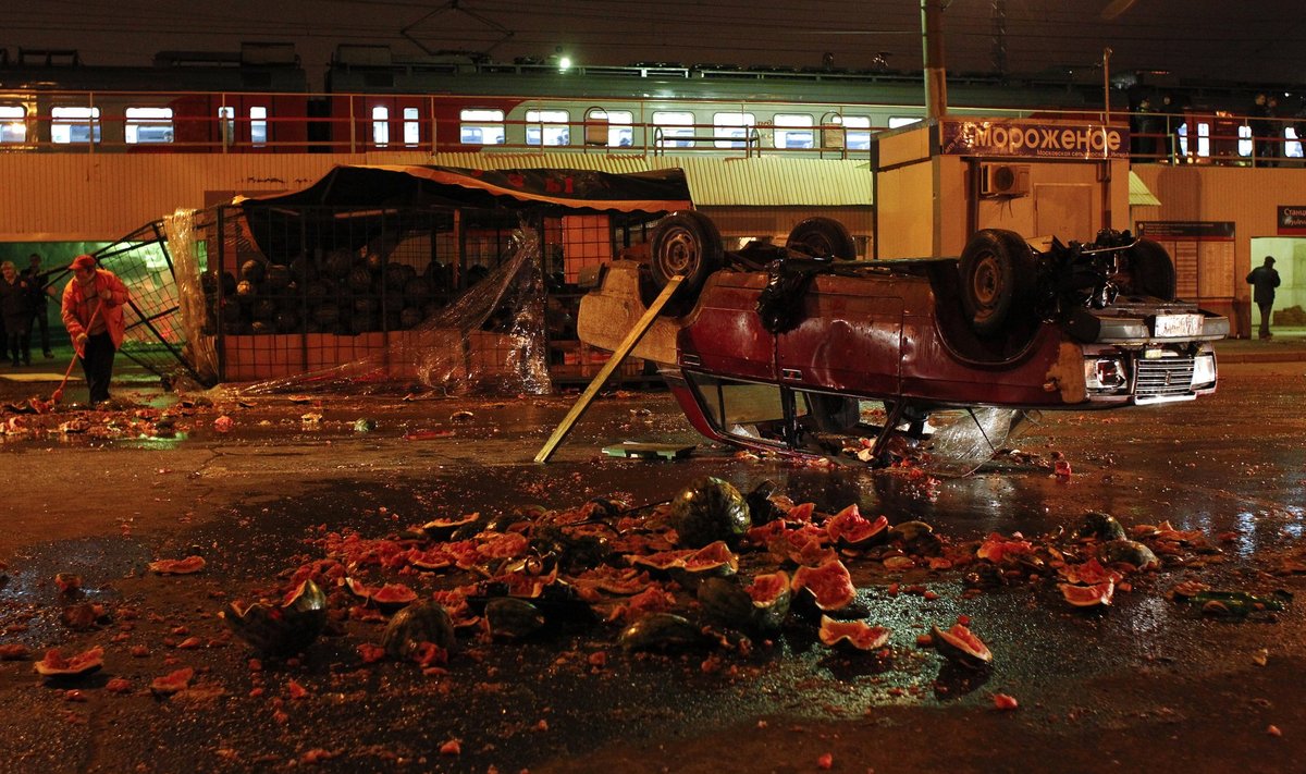 A man clears up near an overturned car and smashed watermelon stand after a protest in the Biryulyovo district of Moscow