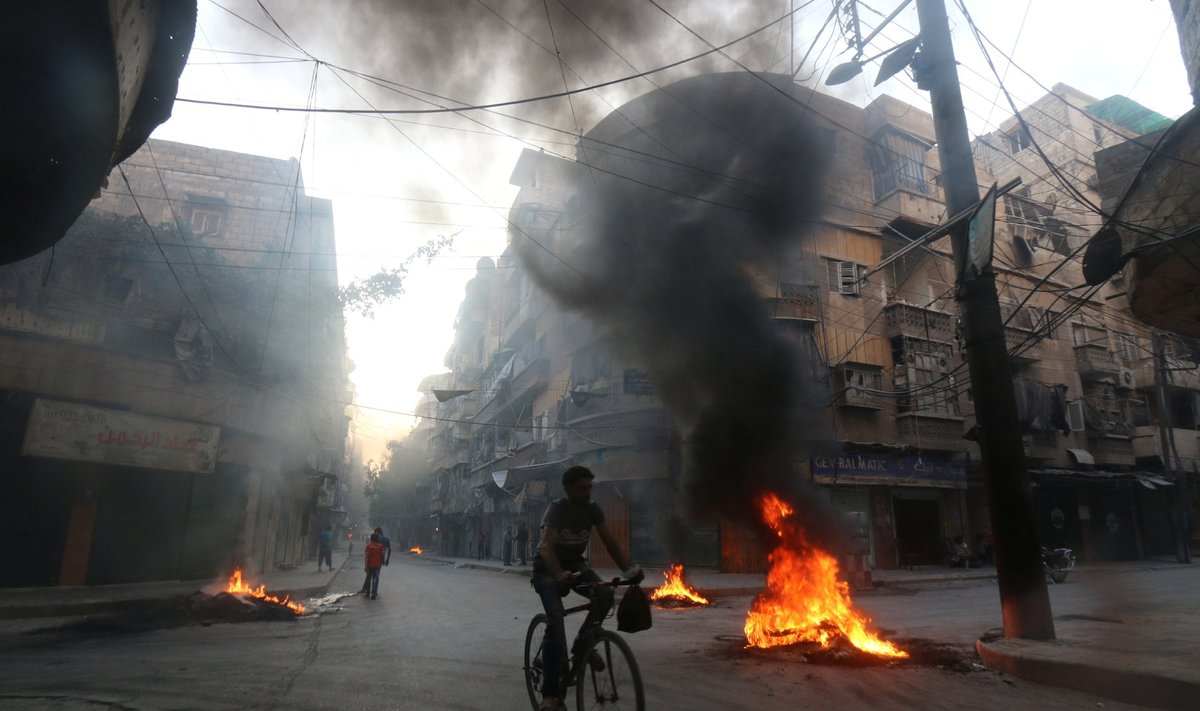 A man rides a bicycle past burning tyres, which activists said are used to create smoke cover from warplanes, in Aleppo