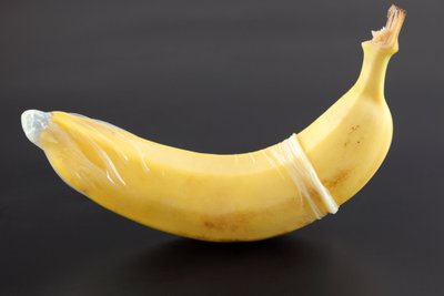 Banana with condom on black background