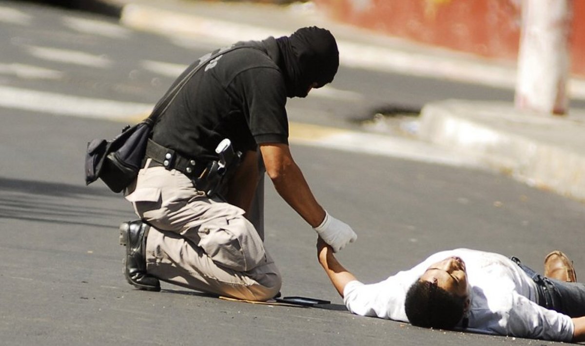 Maskeeritud politseinik uurib palgamõrvari ohvrit El Salvadoris.