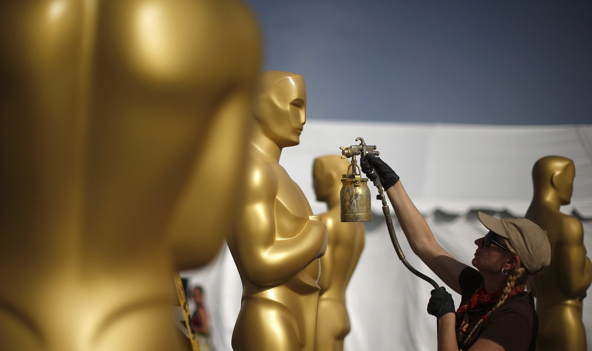 A woman spray paints Oscar statues in a parking lot in preparation for the 87th Academy Awards in Hollywood