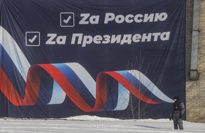 Politseinik valvab Himki suusamaratonil Venemaale ja presidendile austust avaldavat plakatit.