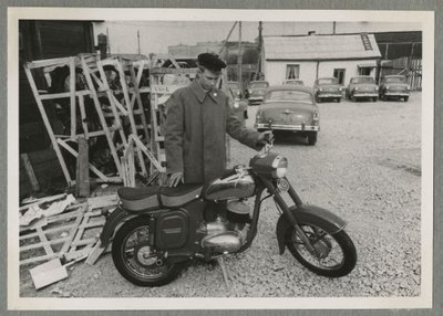 Noormees Endel uut mootorratast ostmas. Kõrval kastides mootorrattad ja taustal autoparkla sõiduautodega.