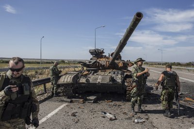 Pro-Russian rebels stand near a burnt-out Ukrainian tank outside the destroyed airport in Luhanks
