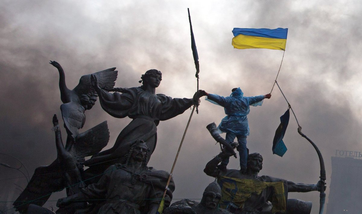 An anti-government protester waves the national flag from the top of a statue during clashes with riot police in the Independence Square in Kiev