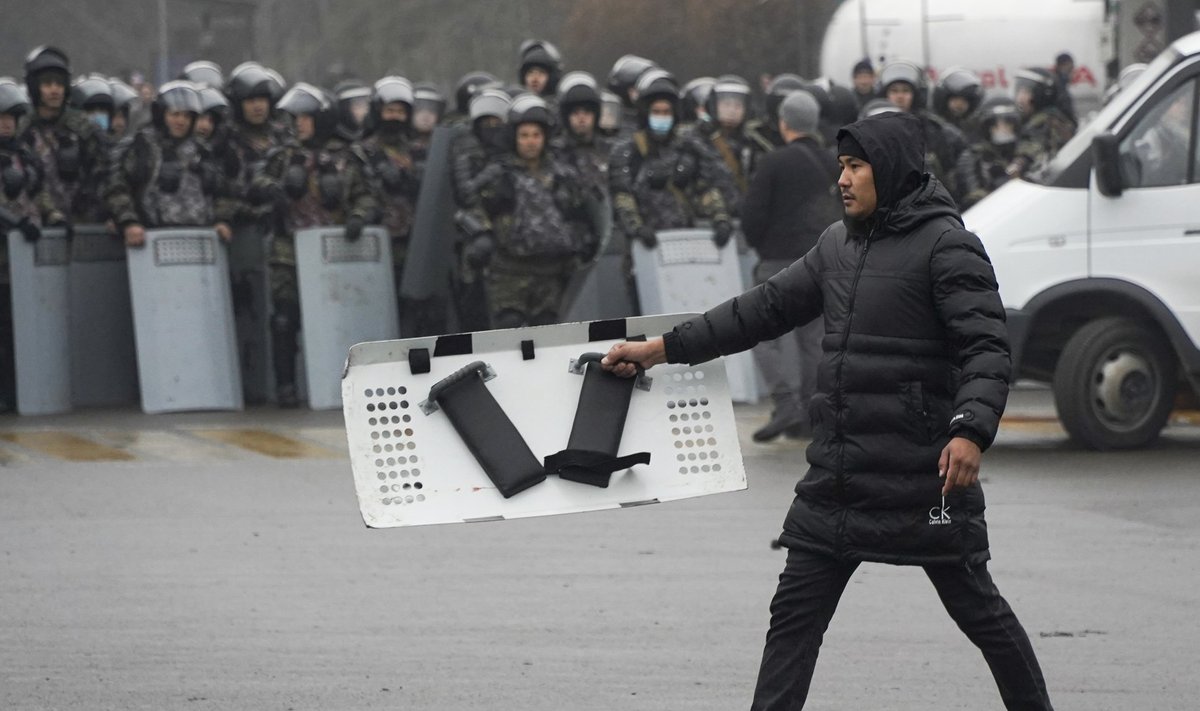 Meeleavaldaja uhkustab Almatõs märulipolitseilt võetud kilbiga, politseinikud vaatavad pealt.