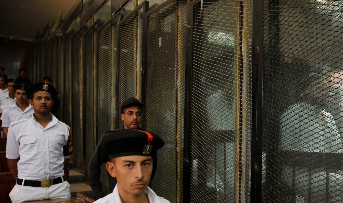 Police officers stand guard as defendants accused of involvement in the 2015 assassination of Egypt's top prosecutor are seen in a cage in a courtroom, on the outskirts of Cairo