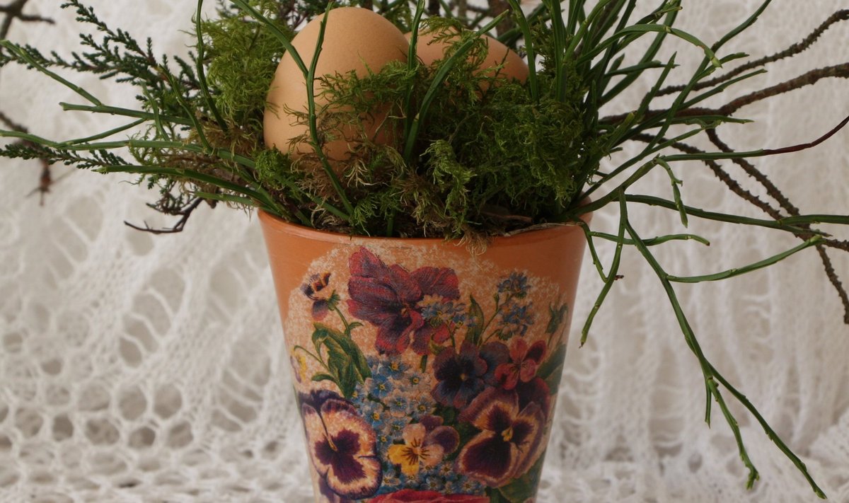 Vanale vaasile on kantud lilleline pilt. Pange vaasi pisut sammalt ja oksi ning sinna sisse peitke munad.
