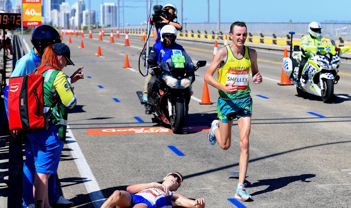 Scotland's Callum Hawkins lies on the ground as Australia's Michael Shelley runs past during the Men's Marathon at the Commonwealth Games on the Gold Coast