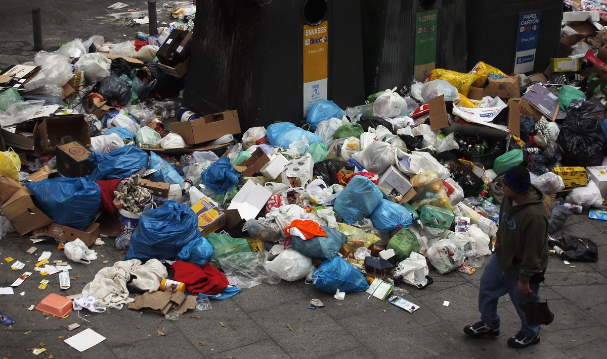 A man walks past garbage strewn on the pavement on the fourth day of an indefinite strike by street cleaners in central Madrid