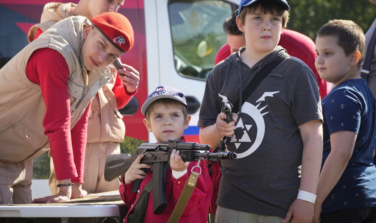 Дети позируют для фото с оружием в передвижном призывном пункте во время празднования Дня России в парке Санкт-Петербурга.