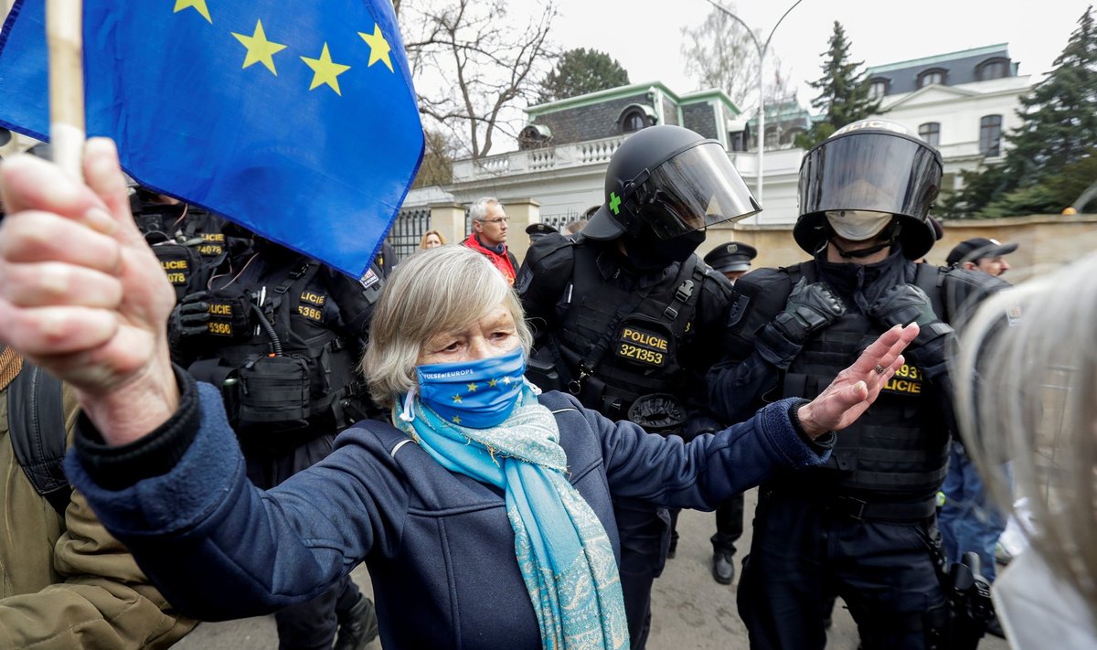EL-i lipuga meeleavaldaja Praha Vene saatkonna ees politseiametniku kõrval. Meeleavaldused algasid, kui selgus, et 2014. aasta Vrbětice lõhkeainelao plahvatuse korraldas Venemaa luureteenistus.