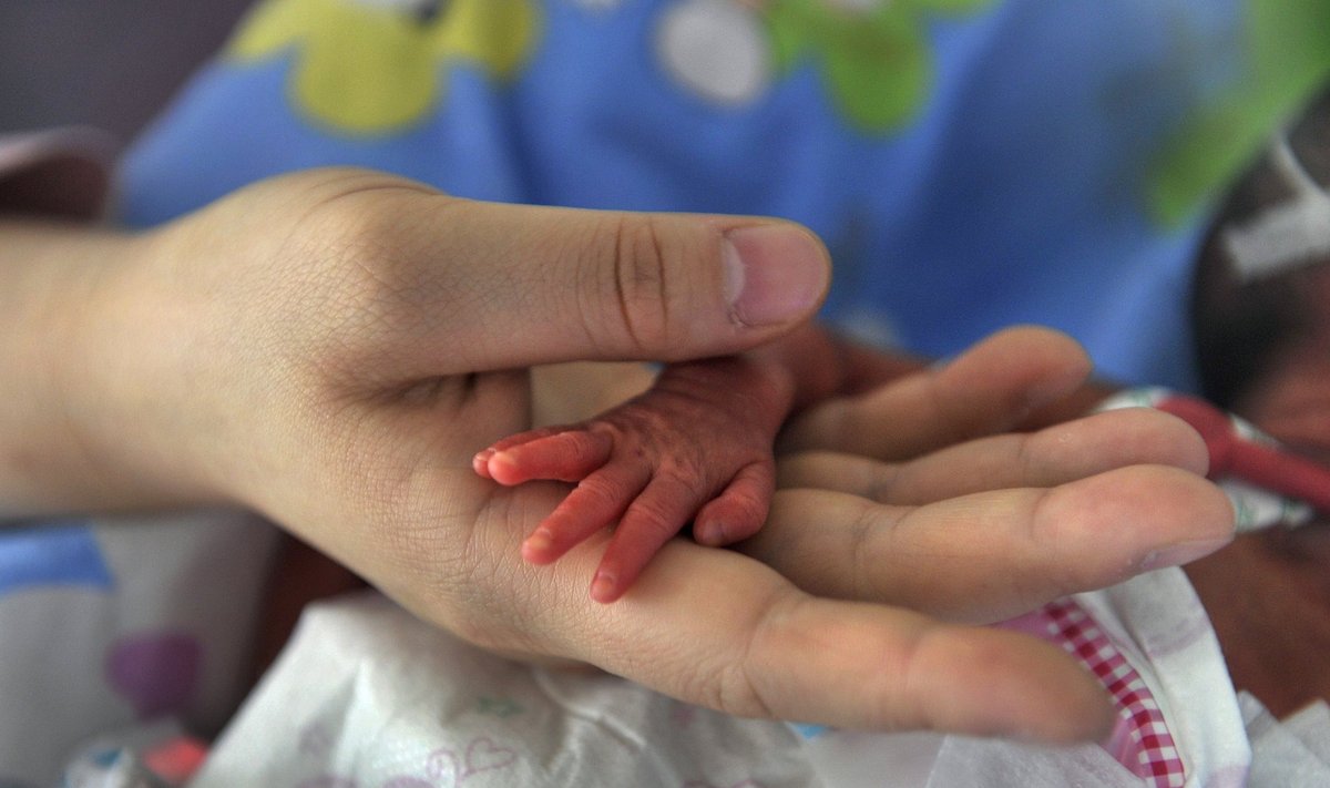 A nurse holds the hand of a premature baby girl lying in an incubator at a hospital in Chongqing