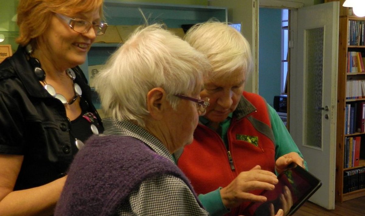 E-lugerit katsetavad raamatukogu juhataja Ilme Säde silma alla eakad lugejad Elsa Jans ja Merike Asku.
