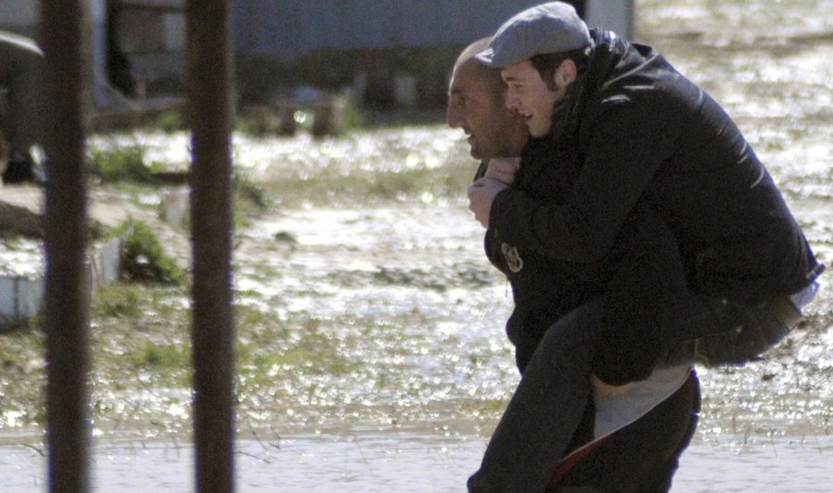 A man carries his neighbour across a flooded street at a refugee settlement outside Tbilisi March 16, 2010. After heavy rains in the region some settlements in Georgia were flooded. REUTERS/Nodar Tskhvirashvili (GEORGIA - Tags: DISASTER ENVIRONMENT)