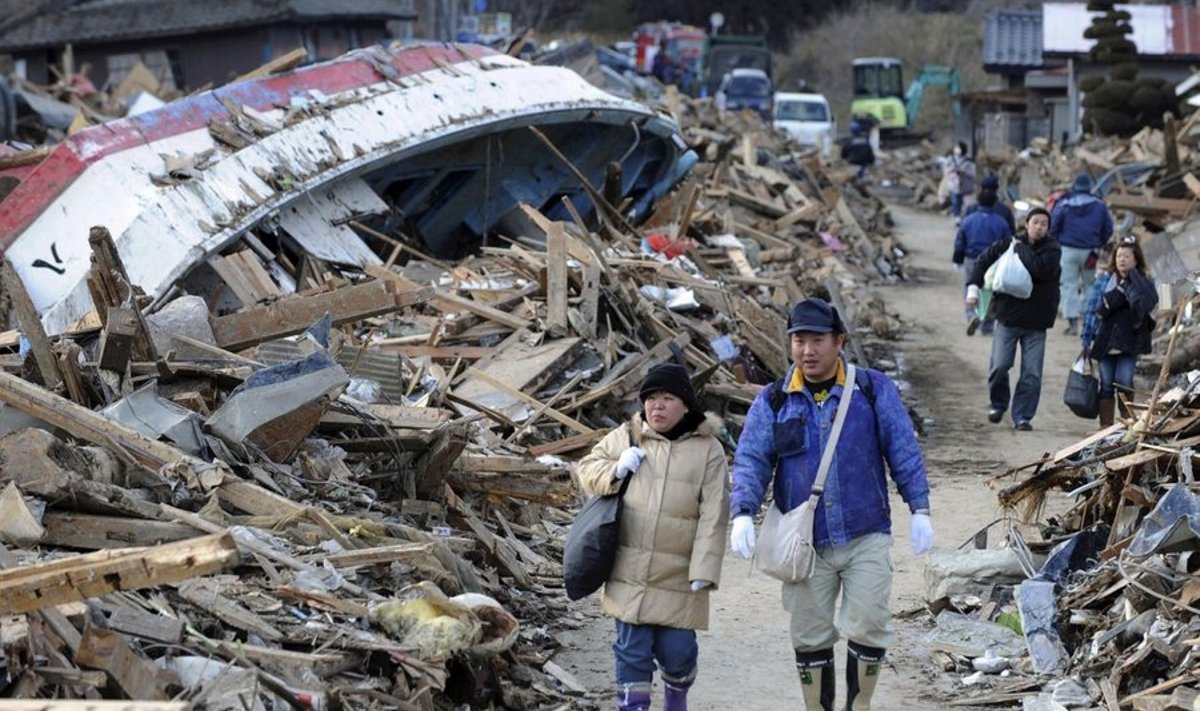 Local residents walk past debris, including an overturned fishing boat, in the town of Minamisanriku in Miyagi prefecture on March 12, 2011 
