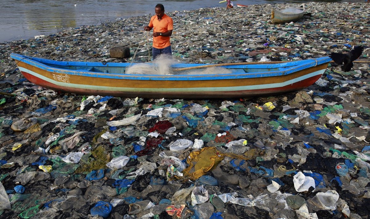 India kalamees Mumbai lähedal kilekotte täis meres oma võrku ette valmistamas.  