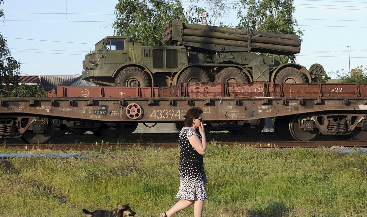 A multiple launch rocket system is seen on a freight train platform as a woman and a dog pass by in Matveev Kurgan