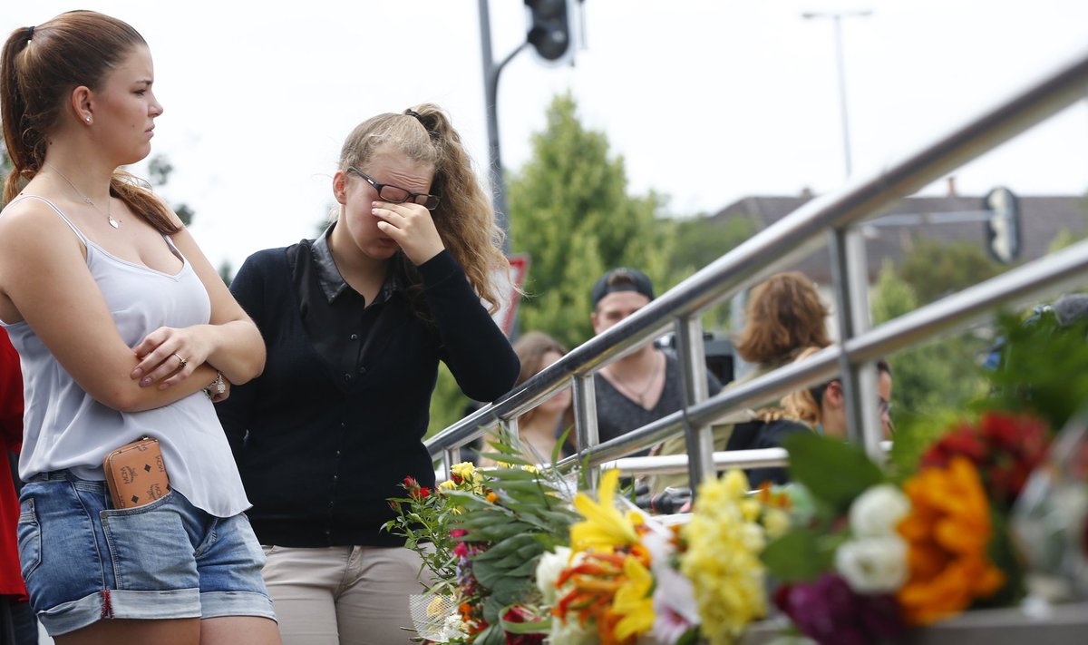 Young women look at floral tributes near Olympia shopping mall in Munich