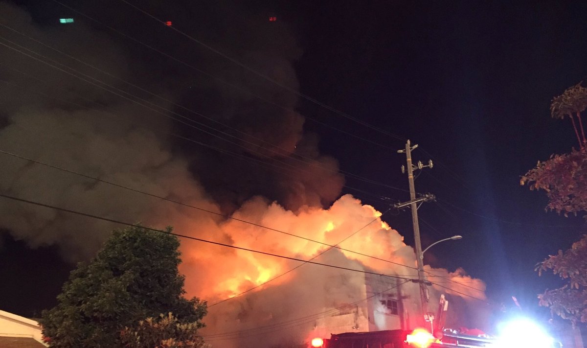 Flames rise from the top of a warehouse, which caught fire during a dance party in Oakland