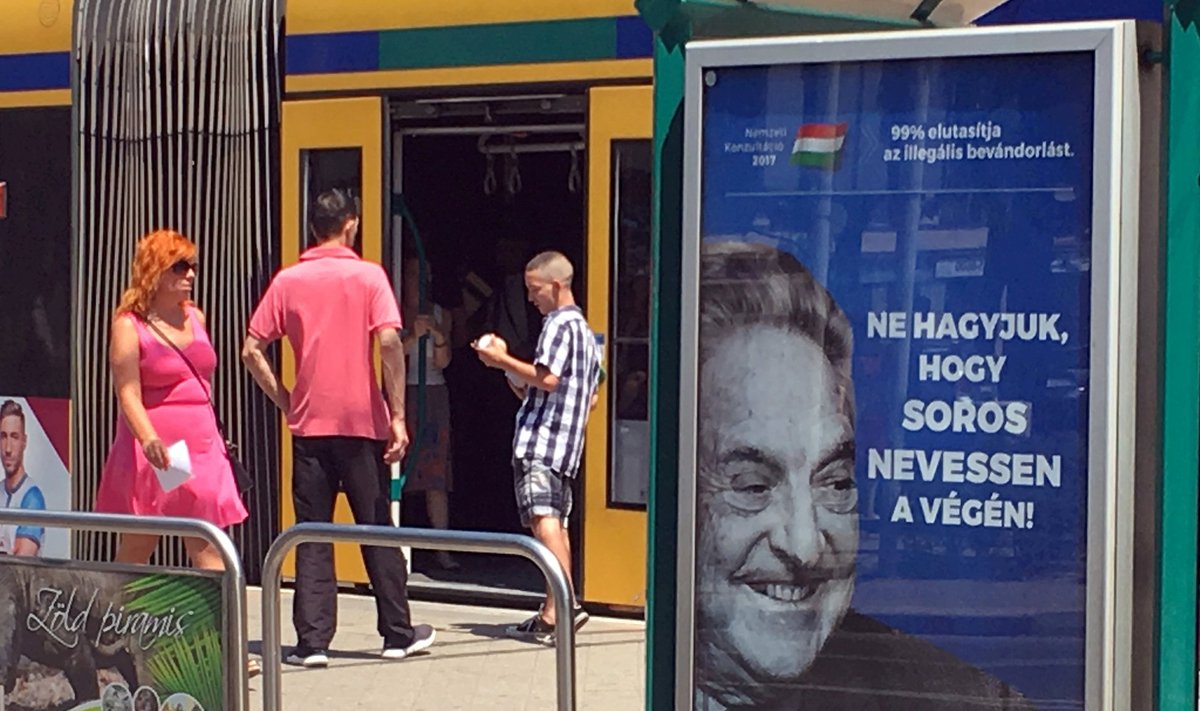 Budapesti trammipeatustes jälgib ungarlasi Sorose saatanlik irve.