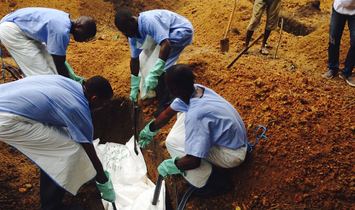 Volunteers lower a corpse, which is prepared with safe burial practices, into a grave in Kailahun