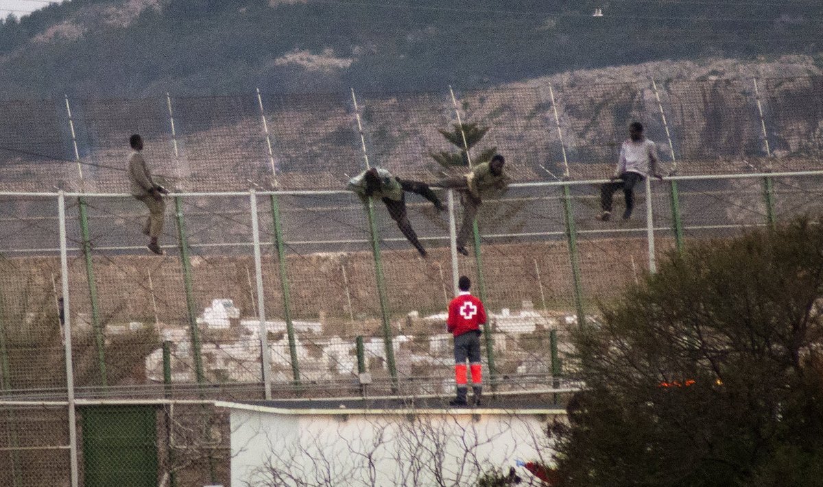 Migrandid sisenemas Melilla enklaavi, Punase Risti töötaja valmistub neid abistama.