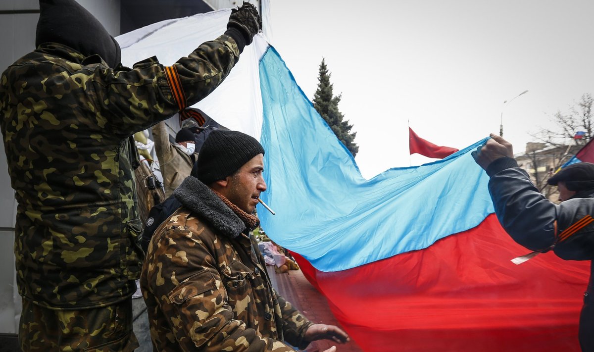 A pro-Russian protester warms himself by a stove as fellow protesters raise a Russian flag during a rally in Luhansk