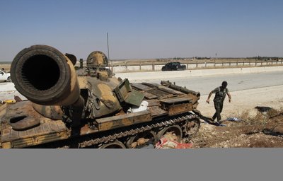A Free Syrian Army fighter walks past a damaged tank and a dead body outside the Minnig Military Airport
